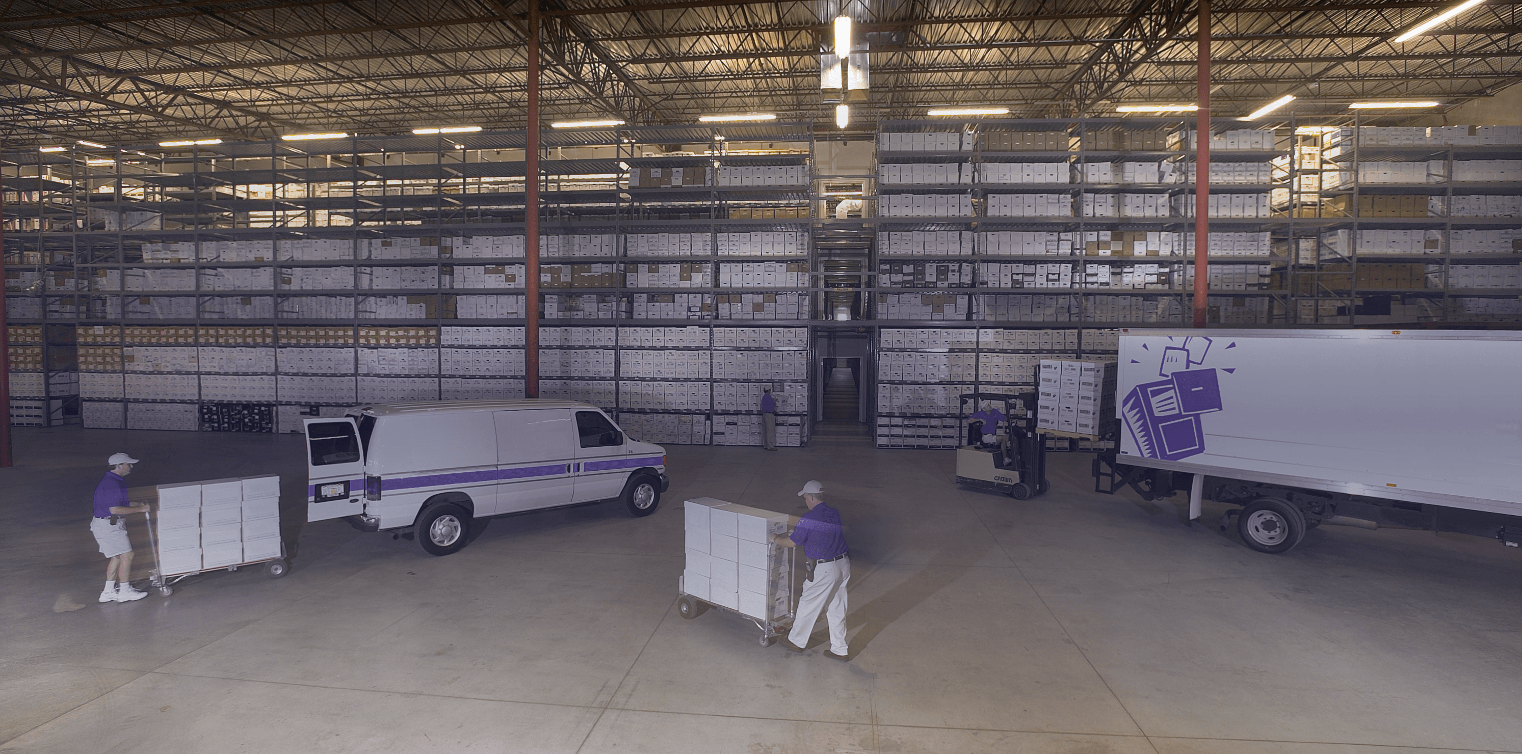A busy records management warehouse with workers transporting document storage carts between trucks and shelves.