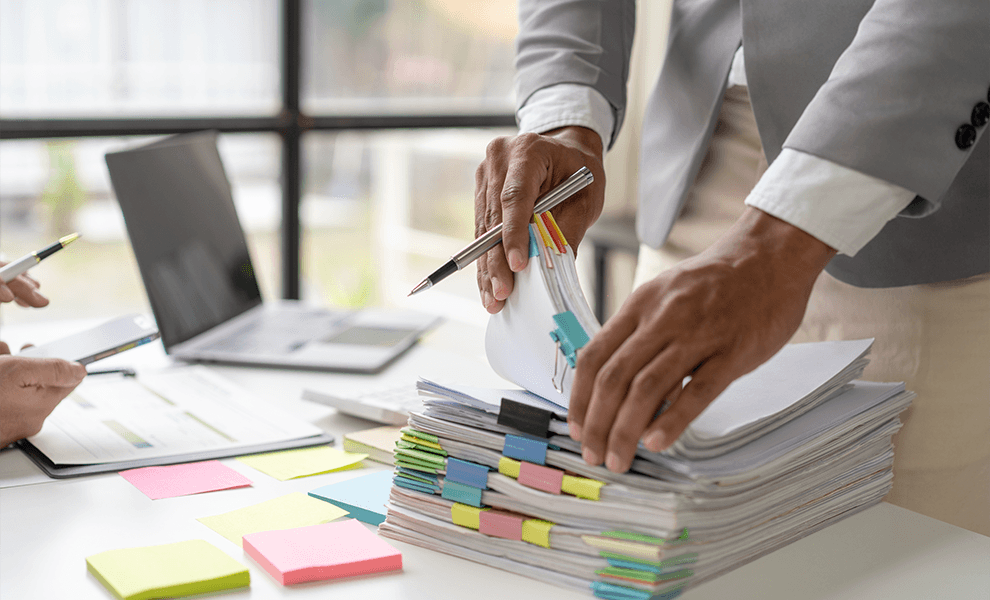Two financial workers collaborating on a stack of organized financial records, managing their stored records on the Annex platform on their phones. 