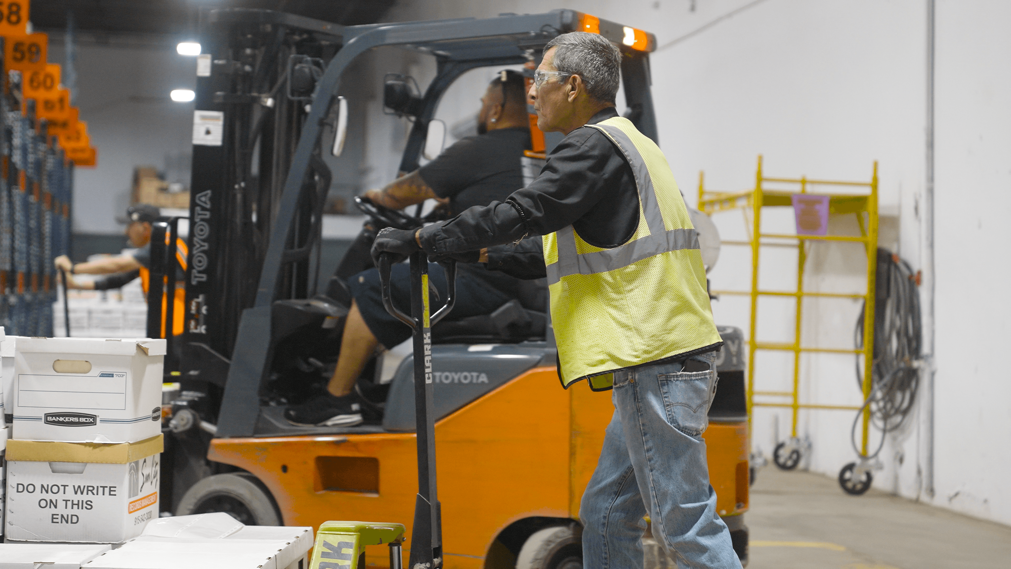 Employees in a secure records management facility organize and transport document storage boxes, ensuring efficient handling and retrieval in a high-volume warehouse.